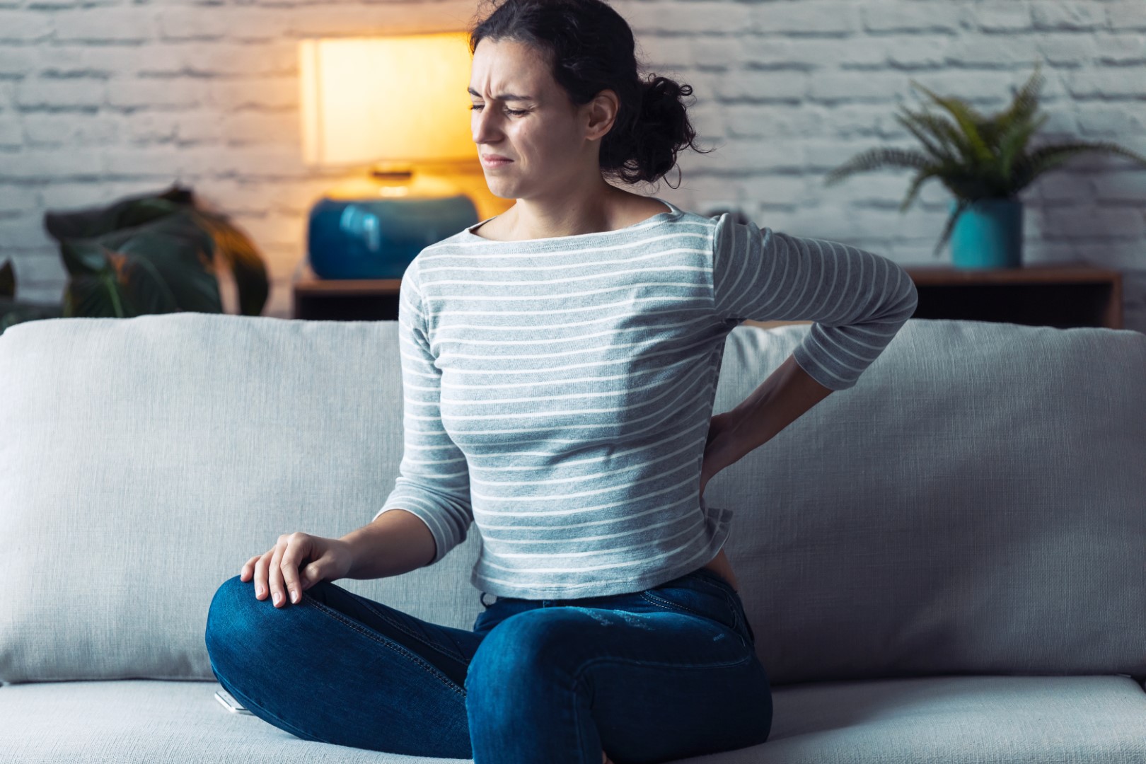 Young woman with back pain sitting on the sofa in the living room