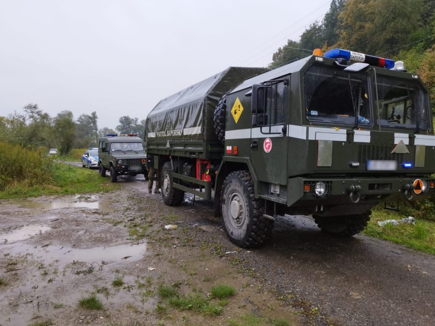 dwa pojazdy patrolu saperskiego, za nimi oznakowany radiowóz policji