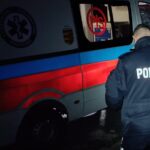 noc, policjant stoi obok karetki, dalej zaparkowany policyjny radiowóz