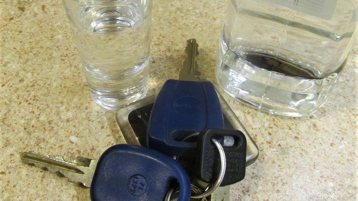 kluczyki do samochodu, obok kieliszek i butelka z alkoholem