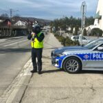 policjant ruchu drogowego z laserowym miernikiem prędkości, obok oznakowany radiowóz