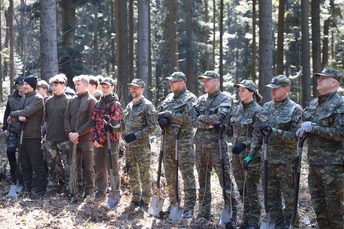 Line of soldiers and trainees in camouflage standing in a forest, each holding a shovel for outdoor work or training. (Informative)