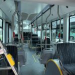 Interior of an empty city bus with rows of dark seats, metal handrails, and big windows; yellow priority seating and obvious aisle leading toward the front.
