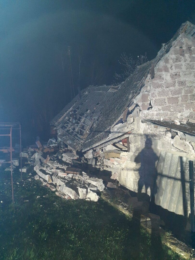 Ruined stone building with a collapsed roof and scattered bricks at night, with a long shadow of a person in the foreground.
