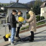 Two boys handing a bouquet of bright yellow flowers to a woman on a sunny outdoor walkway.
