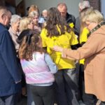 A crowd of adults and children gathered near the doorway of a building, several people wearing bright yellow shirts.