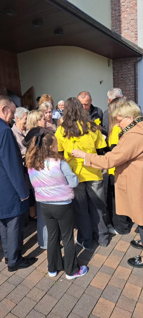 A crowd of adults and children gathered near the doorway of a building, several people wearing bright yellow shirts.