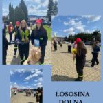 Firefighters in uniform handing out potted plants to children at an outdoor community event in Lososina Dolna on a sunny day.
