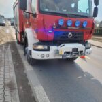 Front view of a red fire truck parked on the road, with blue emergency lights and a heavy bumper assembly visible in the foreground.