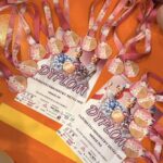Awards laid out on an orange floor: pink-ribbon medals and diplomas labeled 'Dyplom' with dancer graphics, from a children's ceremony.