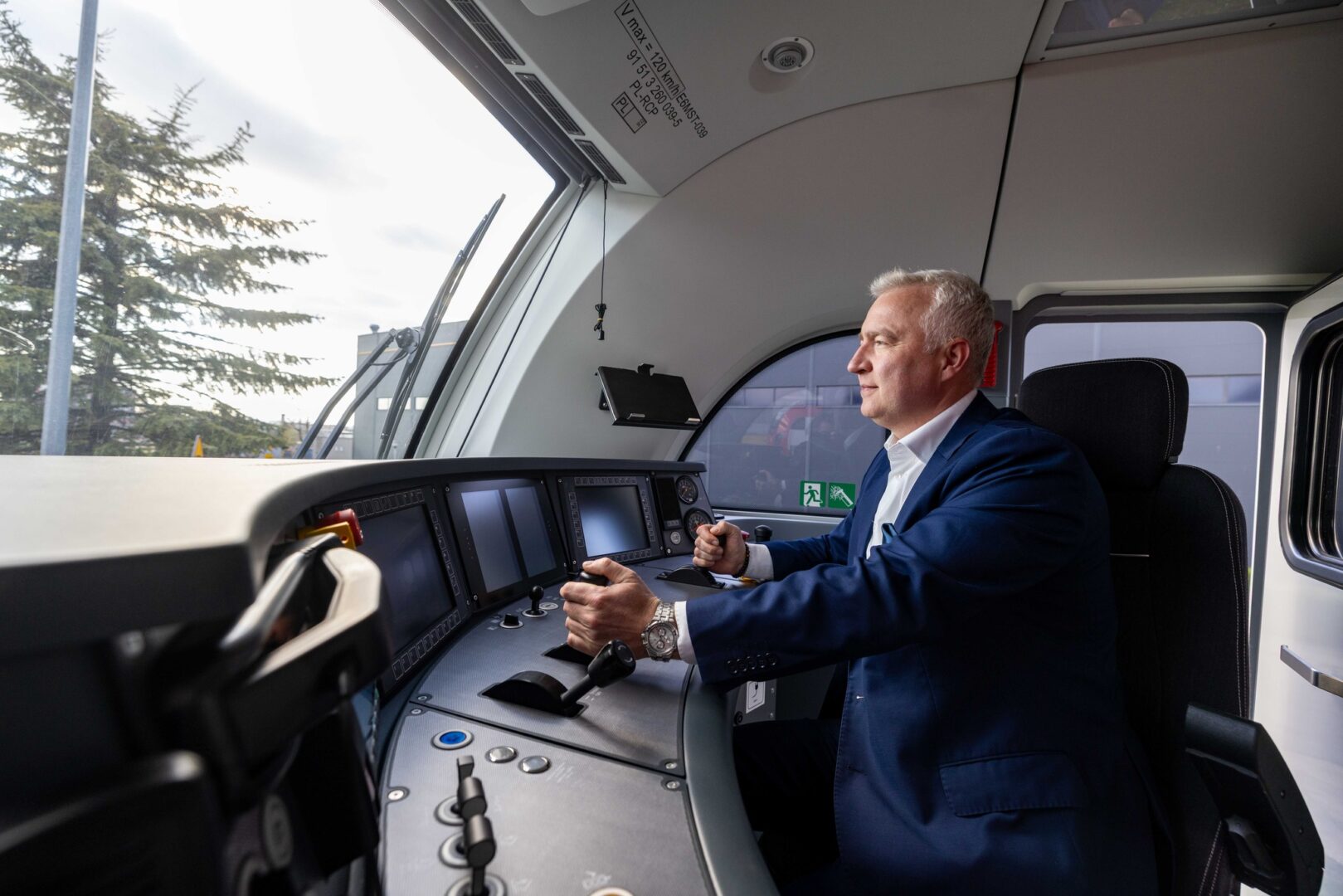 Train engineer in a blue suit operating the cockpit of a modern locomotive.