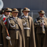 Ceremonial soldiers in brown uniforms with plumed hats, standing with swords and braided cords during a formal parade