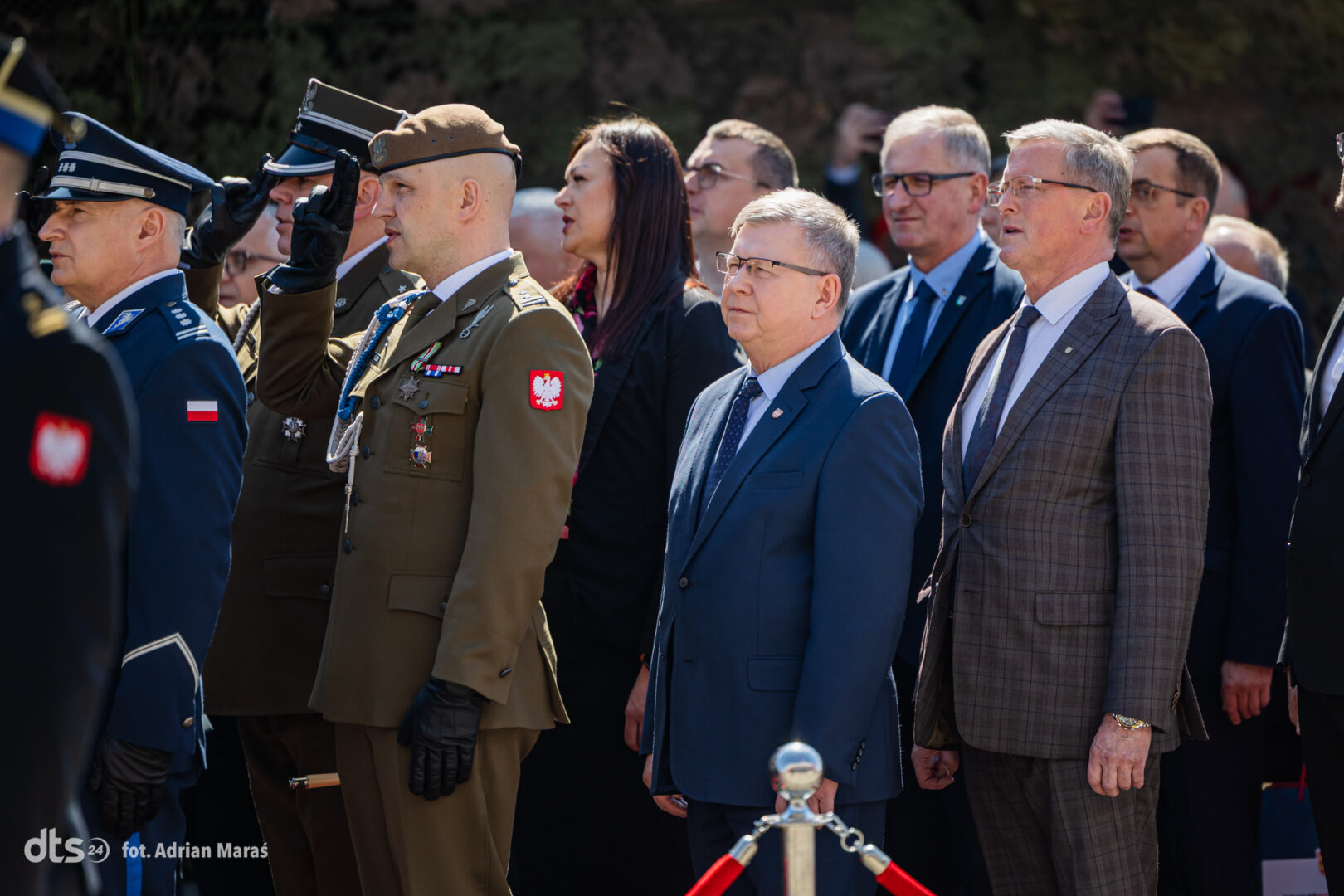 Polish military officer saluting in olive uniform during a formal ceremony, with officials in suits and other uniformed personnel nearby.