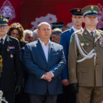 Group of uniformed military officers standing at a formal ceremony, with a man in a blue suit centered among them.