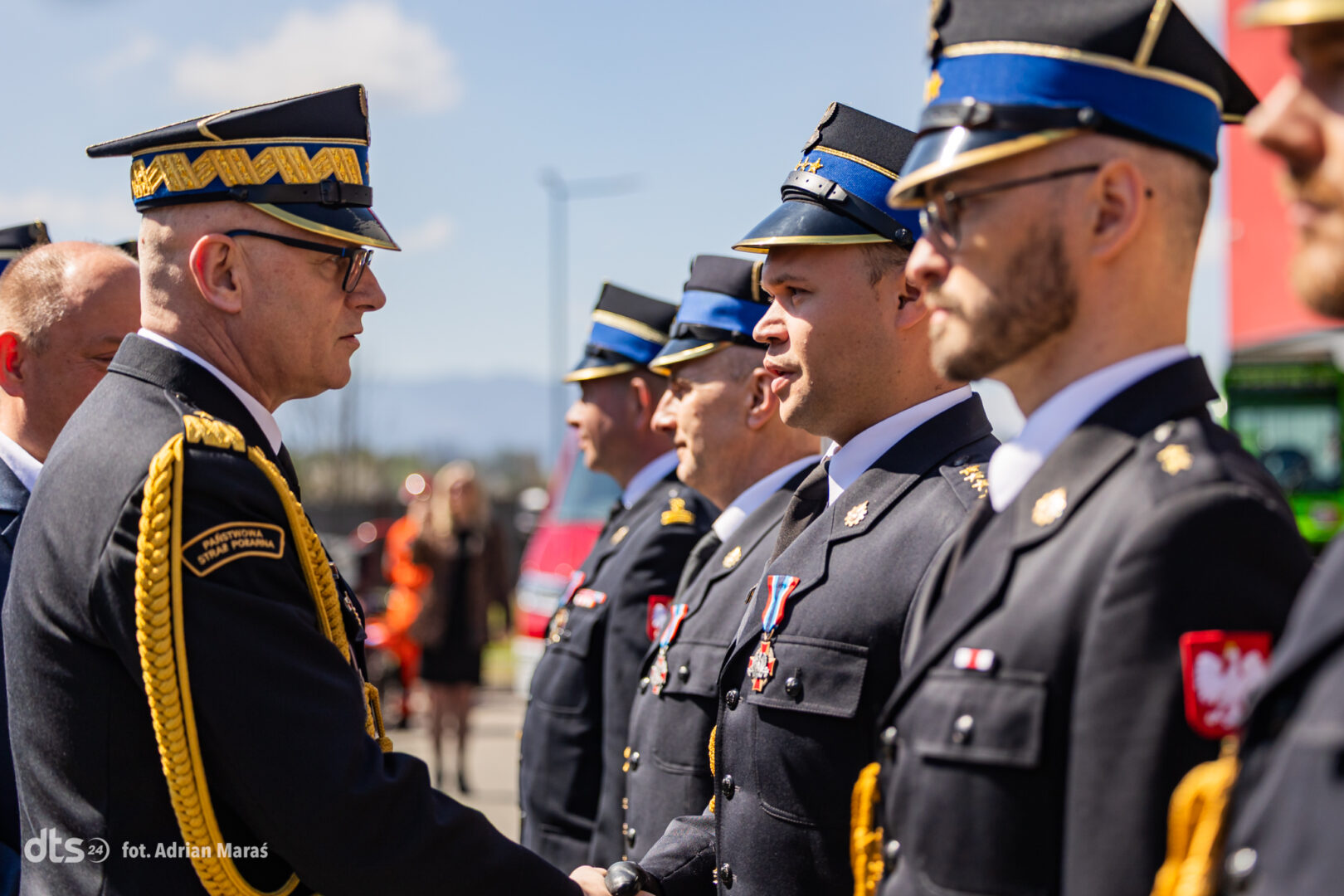 Senior officer in dress uniform shakes hands with a line of uniformed cadets during a formal outdoor ceremony.