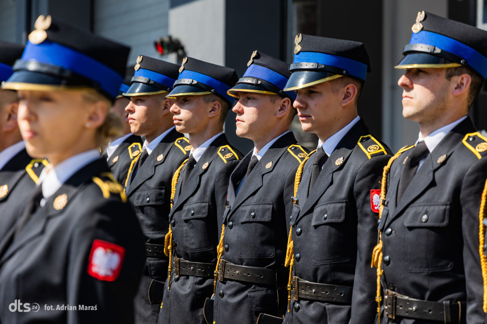 Line of uniformed soldiers standing at attention in black dress uniforms with blue peaked caps and gold trim, Poland patches visible on sleeves
