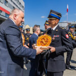 Two uniformed officers exchange a ceremonial flaming emblem during an outdoor military awards event, with other soldiers and spectators in the background.