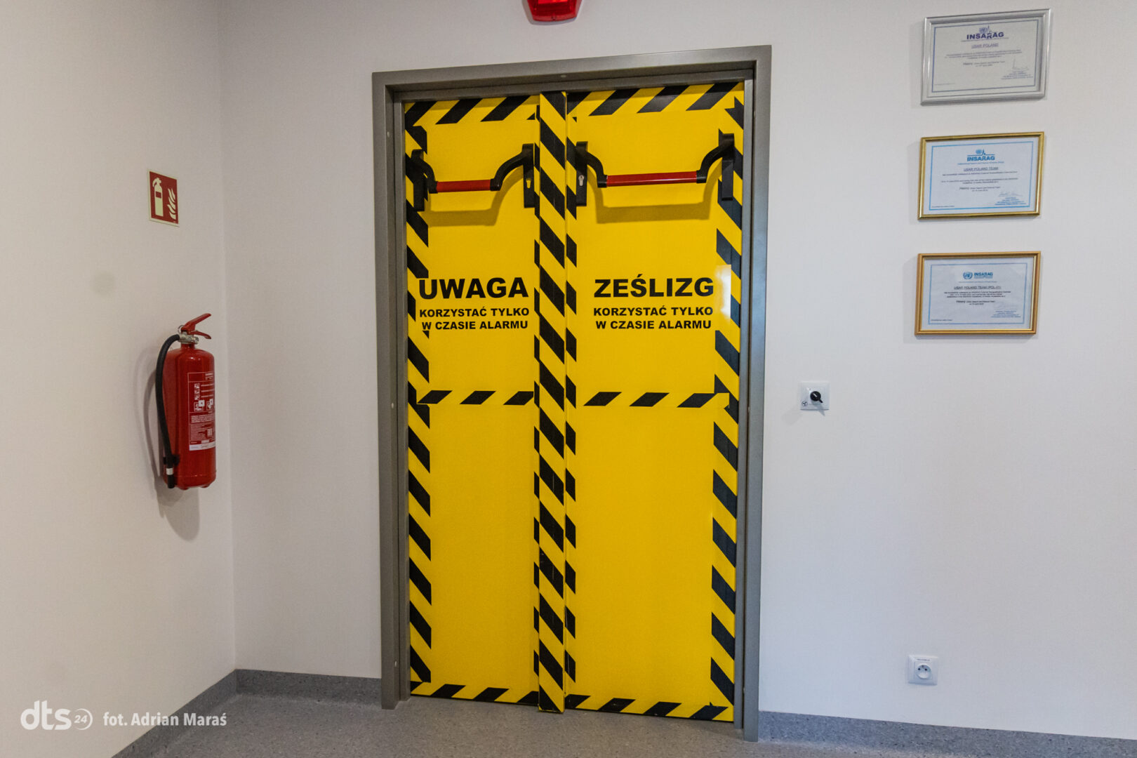 Yellow double emergency door with black diagonal hazard stripes and red horizontal bars; Polish warning to use only during an alarm.