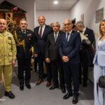 Group of uniformed and civilian officials posing in a hallway during a formal event, with a display structure in the background.