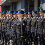 Ceremonial line of uniformed soldiers standing at attention during a parade, wearing dark dress uniforms with blue hats and gold trim