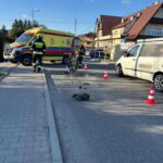 Emergency responders and a yellow ambulance at a street accident, with a toppled motorcycle and traffic cones on the road.