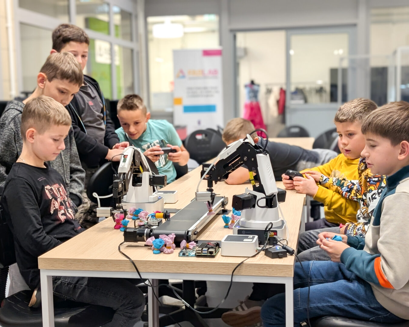Group of boys at a workshop table working with robotic arms and small colorful figures.