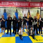 Group of men (and two kids) posing in a martial arts gym with punching bags and a red banner overhead in Chinese.