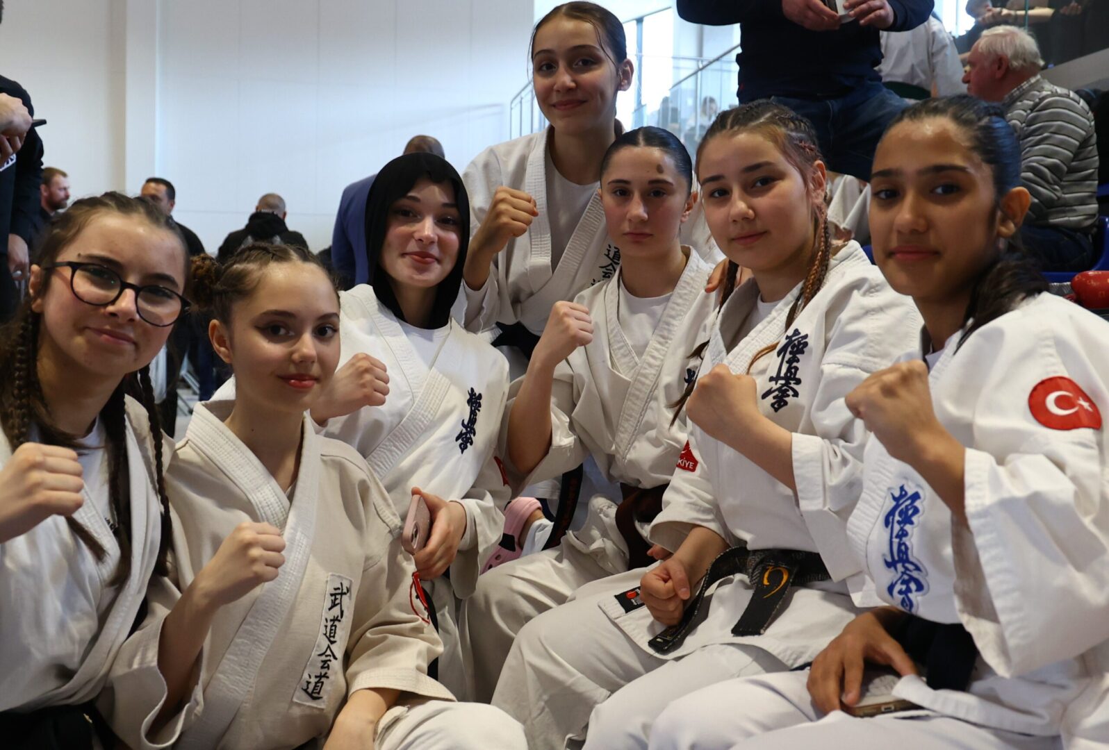 Group of young women in karate gi uniforms posing with fists raised indoors.