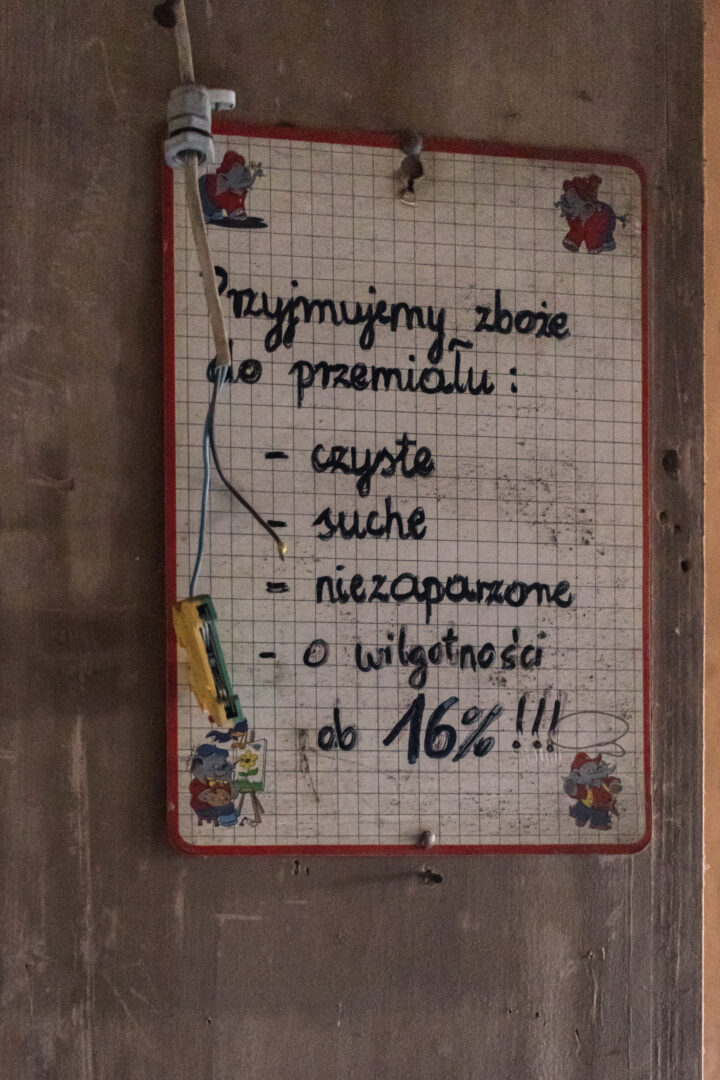 Small wall sign with handwritten Polish list about grain storage: clean, dry, pest-free, moisture under 16% (attached to a wooden surface with wires).