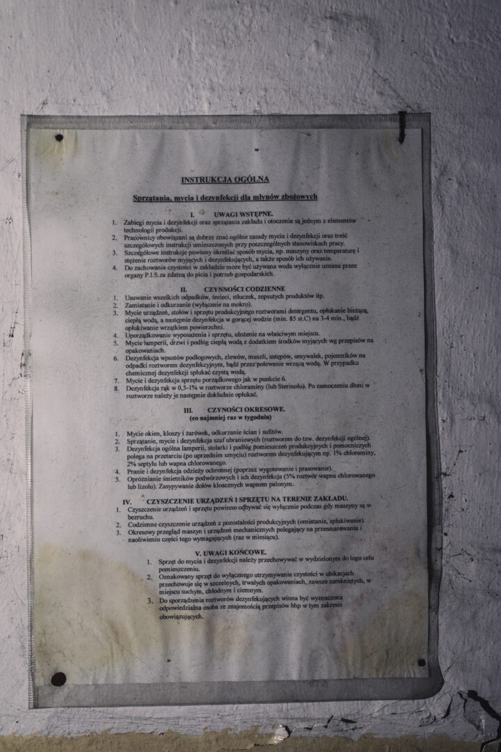 Polish instruction poster titled 'INSTRUKCJA OGÓLNA' on a weathered wall, detailing cleaning procedures for mills in numbered sections.