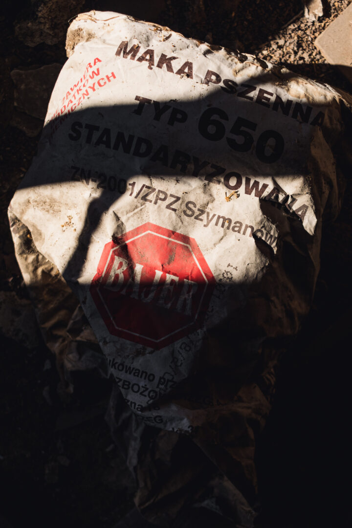 Crumpled white bag labeled 'MĄKA PSZENNA' (wheat flour) with red octagonal 'STOP' sign on a dusty ground surface.
