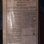 Polish instruction sheet titled INSTRUKCJA mounted on a wooden board, printed in two columns with dense text and a stamp at the bottom right corner.