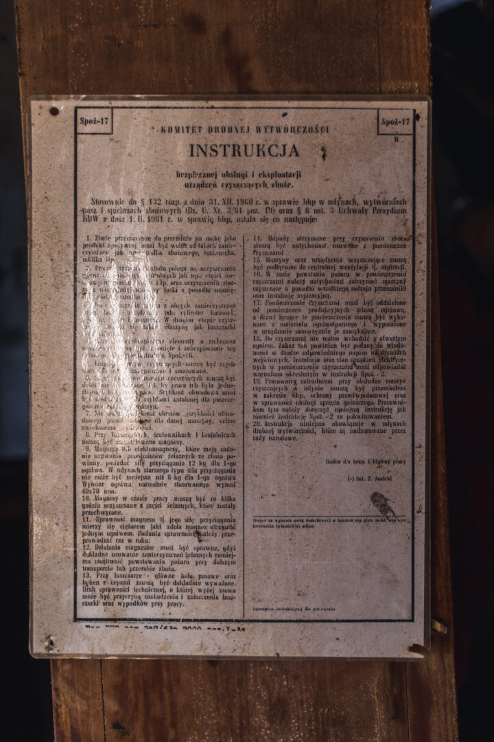 Polish instruction sheet titled INSTRUKCJA mounted on a wooden board, printed in two columns with dense text and a stamp at the bottom right corner.