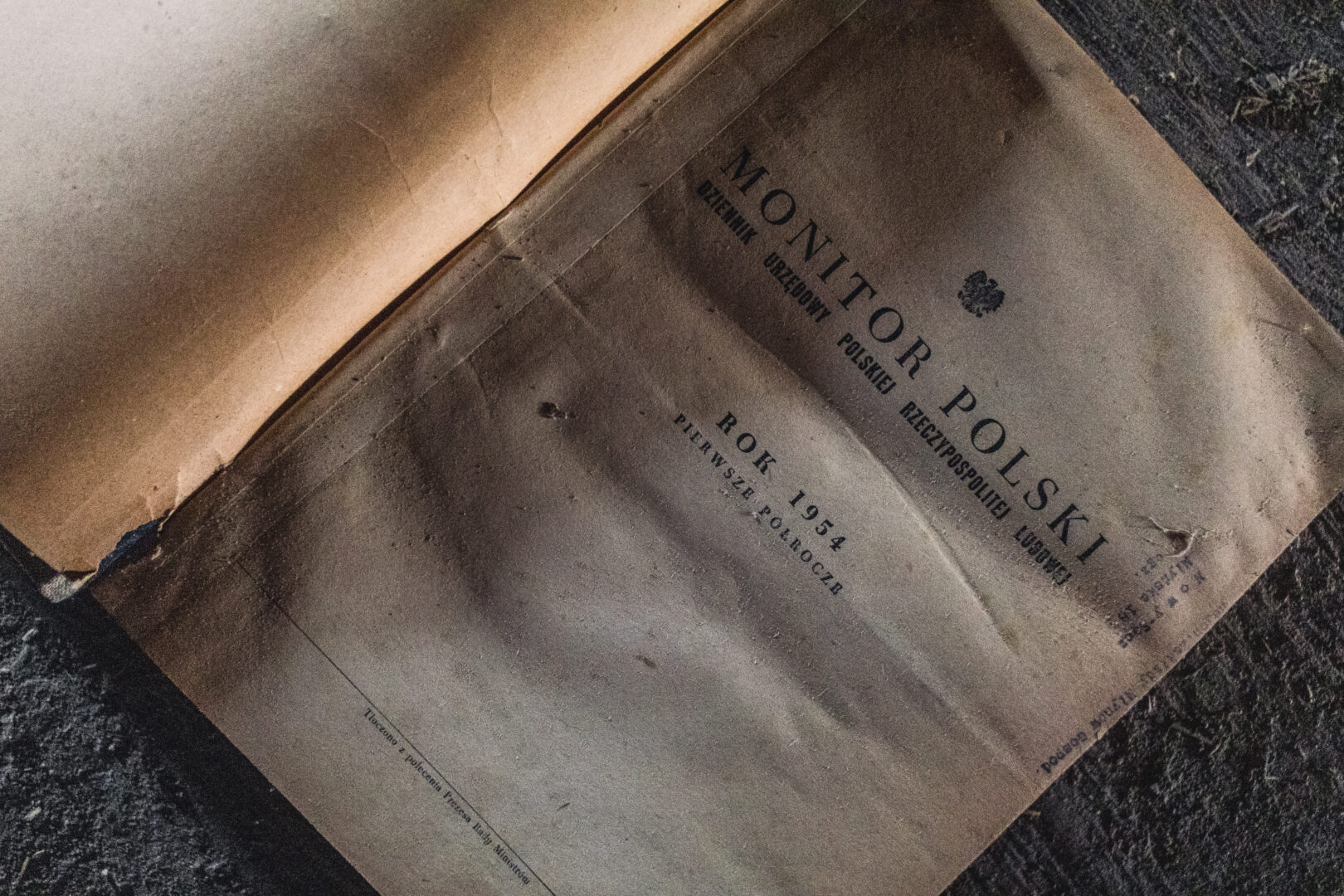 Old Polish government gazette titled 'Monitor Polski' from 1954, dusty and worn on a dark surface.