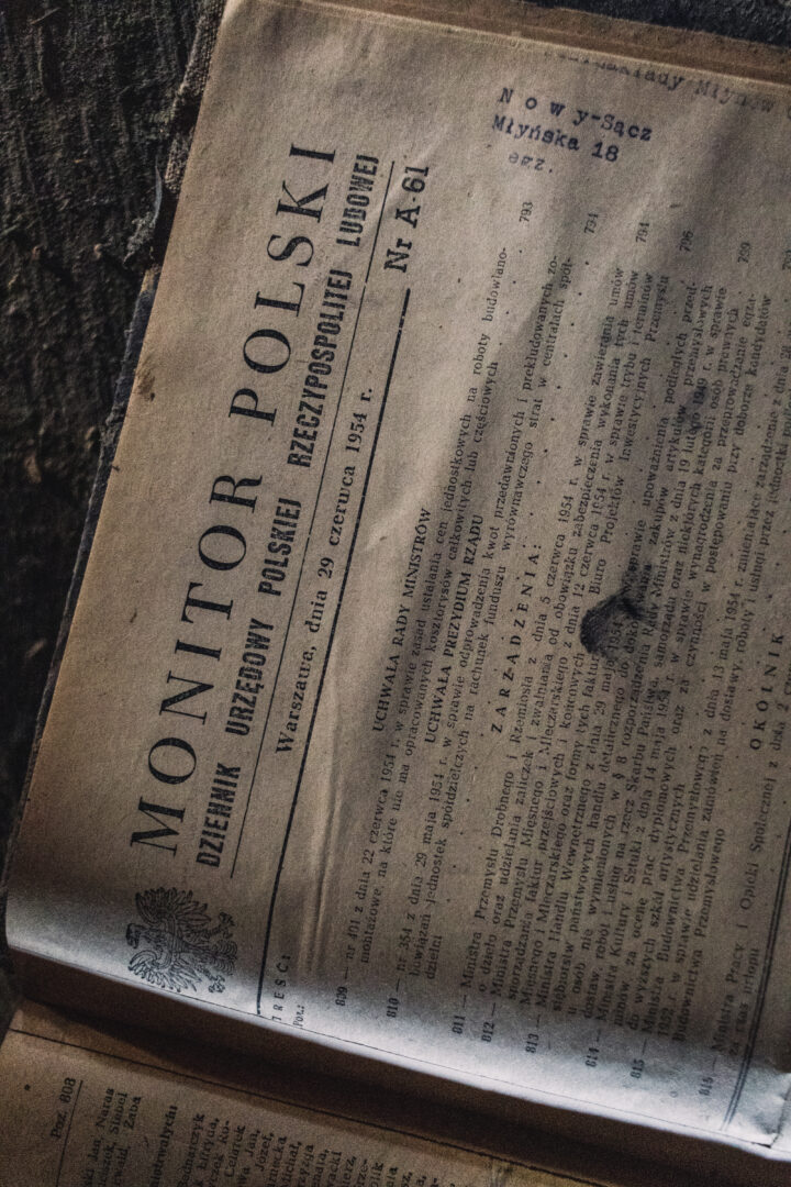 Old Polish newspaper page labeled 'MONITOR POLSKI' with dense columns of text and a decorative crest in the bottom-left corner, photographed at an angle.