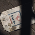 Dusty, weathered envelope on a dark wooden floor with a blue border and red wheat graphic.