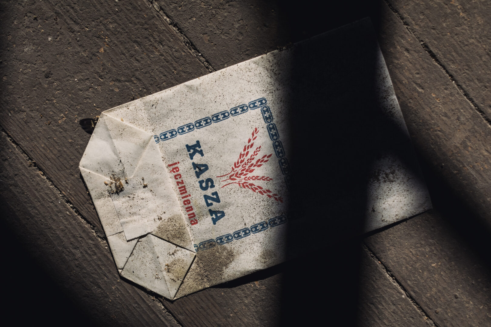 Dusty, weathered envelope on a dark wooden floor with a blue border and red wheat graphic.