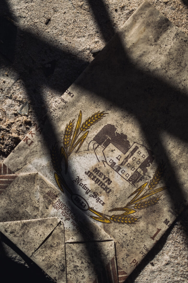 Dusty, torn paper showing a crest with wheat stalks and a building, lying on sandy ground.