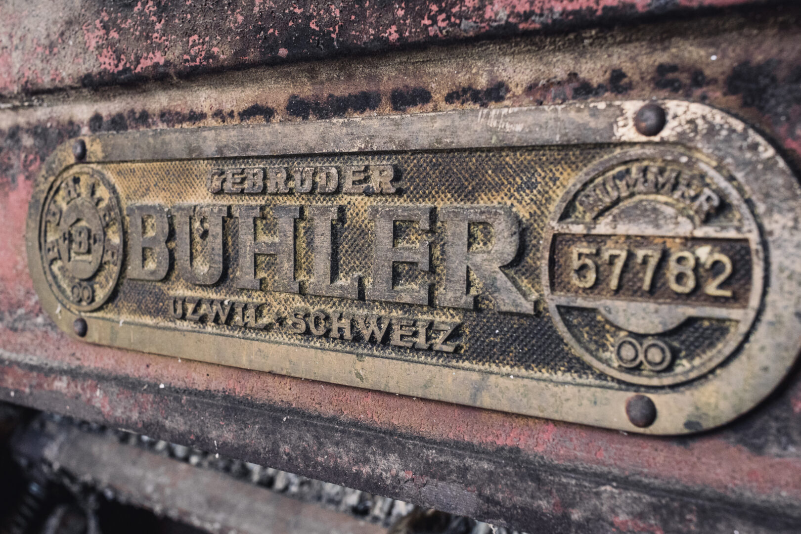 Close-up of a dirty, rusted metal nameplate on a vintage machine, with the large word 'BUTTER' embossed and worn edges nearby.