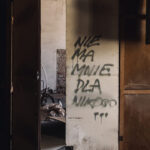 Dimly lit, abandoned doorway with a white metal door covered in black graffiti; piles of debris visible inside.