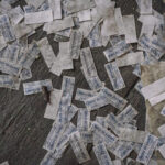 Scattered weathered paper labels on a dark wooden floor, many printed with blue text saying 'CHLEB BULKOWY'.
