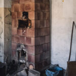 Old brick stove in a dilapidated room with rubble and scattered debris on the floor.
