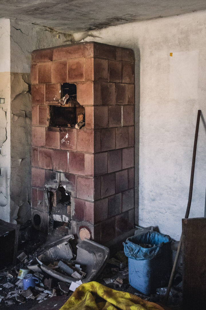 Old brick stove in a dilapidated room with rubble and scattered debris on the floor.