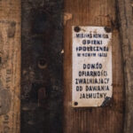 A weathered sign mounted on a wooden wall with Polish text about municipal social care and almsgiving.