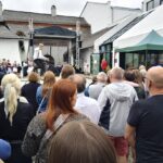 Crowd gathered in front of a small outdoor stage watching a performer in a white shirt.