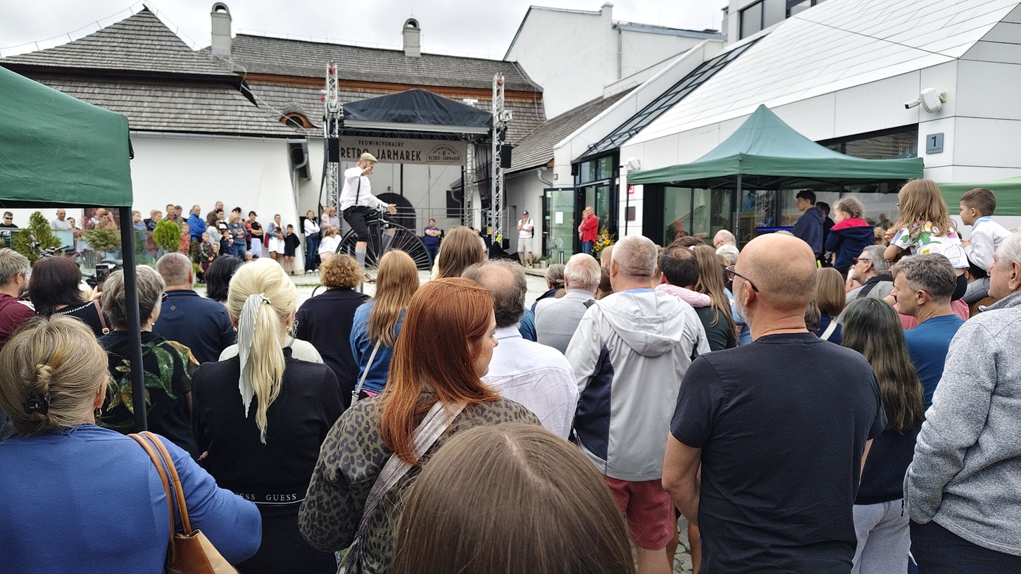 Crowd gathered in front of a small outdoor stage watching a performer in a white shirt.
