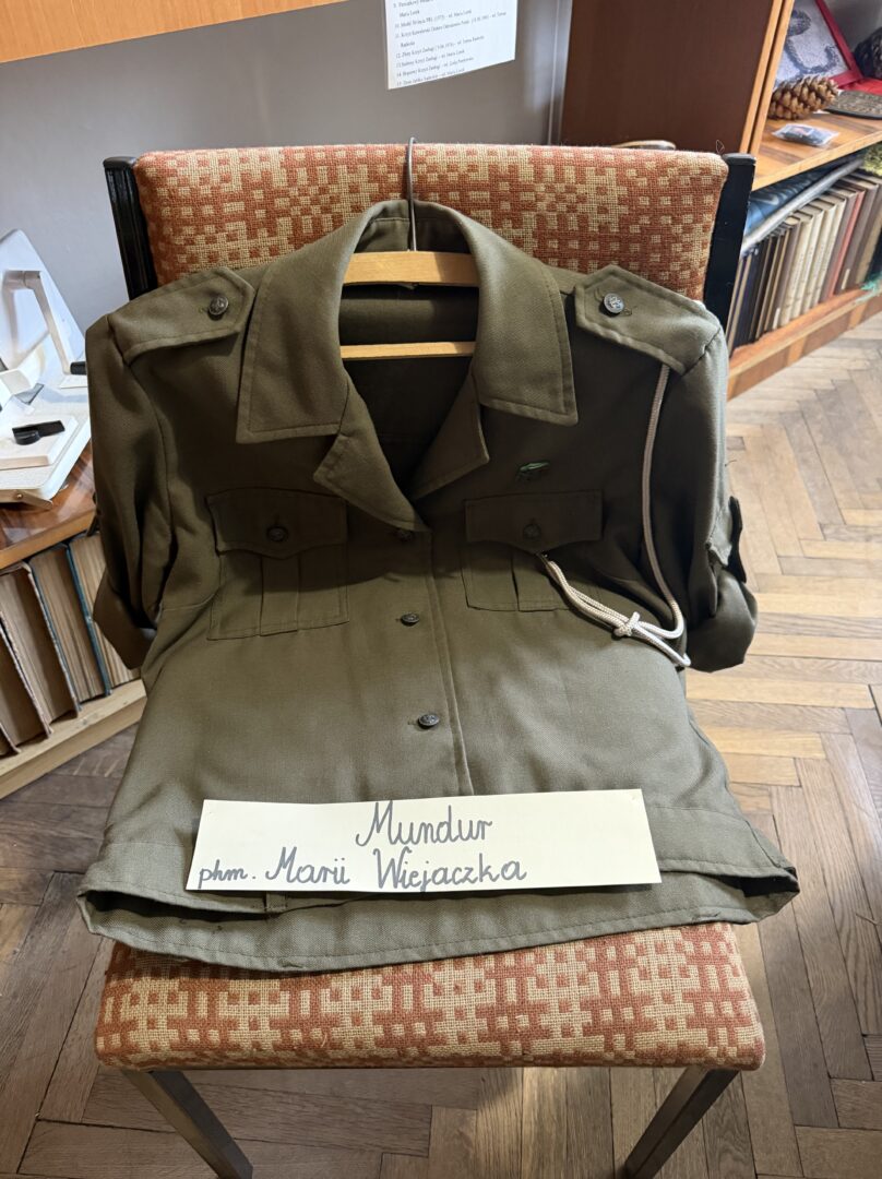 Olive-green military-style jacket draped over a chair with a handwritten sign displaying a name on its lapel area.