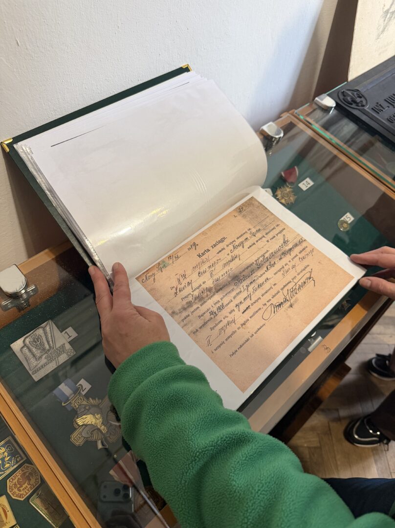 Person in a green sleeve opens a transparent display case to view an old handwritten document in a binder.