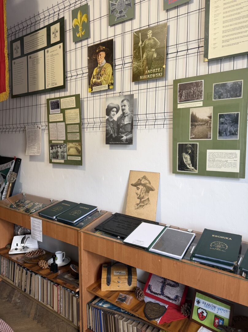 Wall displays with historical photos, plaques, and green panels in a museum case, above wooden shelves of books and artifacts.