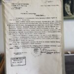 Typed Polish document with stamps, held in a clear plastic sleeve by a person.